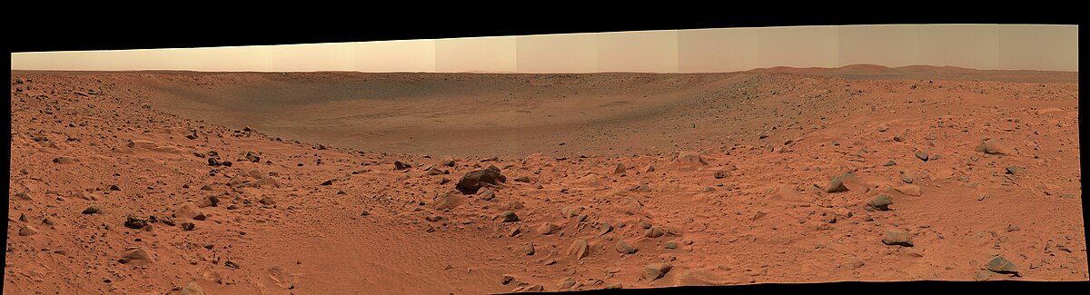 Cratère Bonneville sur Mars : vue sur 180 degrés de la crête extérieure et de l'intérieur du cratère par la caméra panoramique du rover Spirit, le 12 mars 2004 (sol 68). L'éclat de lumière bleu sur le bord opposé du cratère est provoqué par le bouclier thermique de la sonde MER-A, qui s'est détaché lors de l'atterrissage.