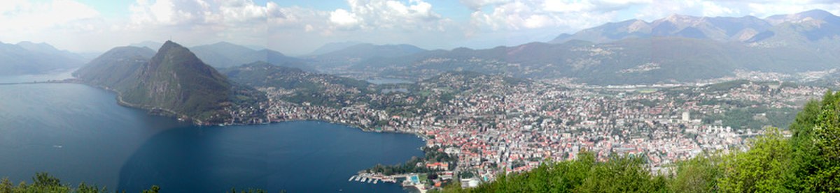 Photo panoramique de Lugano prise de « Monte brè » montrant à gauche: le lac, puis le « Monte San SAlvatore » qui marque l'entrée dans la crique autour de lqauelle s'étend la ville de Lugano