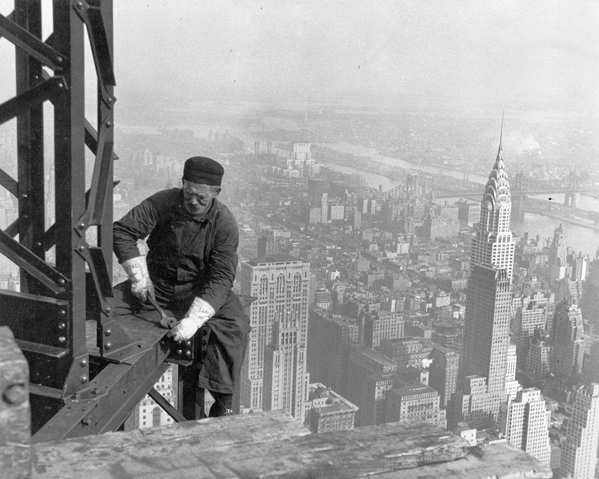 Un skyboy, ouvrier travaillant sur le chantier de l’Empire State Building, sans protection au dessus du vide. Au second plan, le Chrysler Building.