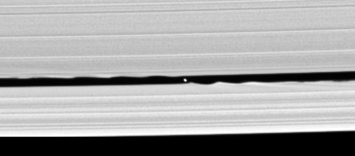 Two bright bands run from the left to right. In the narrow gap between them (Keeler gap), which has wavy edges, a small oblong object can be seen.