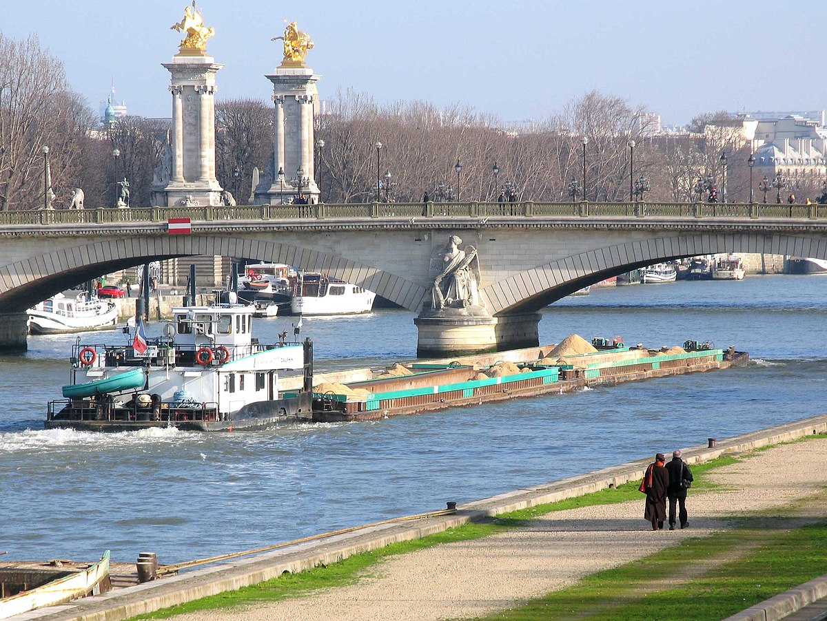 Un pousseur avec 4 barges de sable passe sous un pont de Paris
